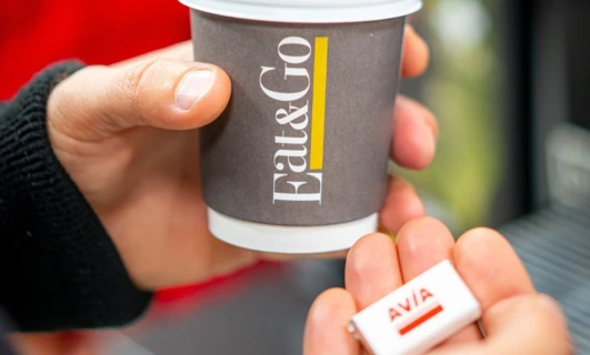 "Owijka na kubek do kawy z logo AVIA i napisem 'Fat&Go' obok kubka z jedzeniem."
