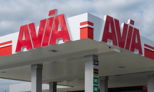 Stacja paliw z różnorodnymi opcjami oleju napędowego dla ciężarówek i SUV-ów, w tym AVA i AVIA. Pojazdy zaparkowane przy pompach z odbijającymi lusterkami.