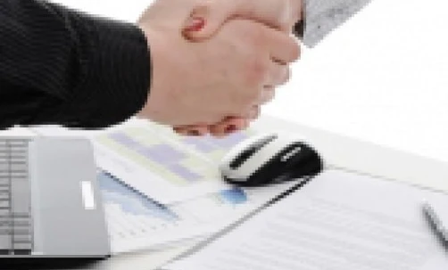 Dwóch pracowników biurowych uściska sobie dłonie w biurze, symbolizując powitanie lub porozumienie między kolegami. Ten gest oznacza profesjonalizm i współpracę podczas spotkania lub dyskusji na temat zarządzania i tematów związanych z pracą.