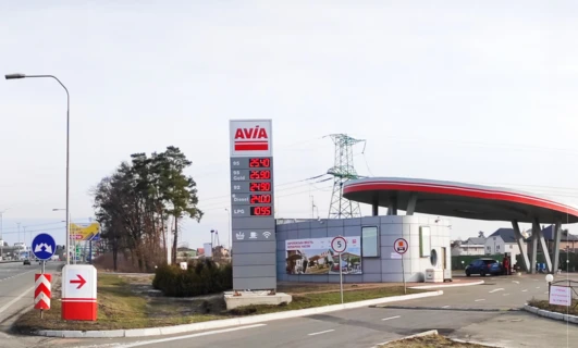 Reklama stacji paliw Avia z cenami benzyny 95 oktanów, Gold, oleju napędowego i LPG. Znak w języku polskim dla Mostu Europejskiego. Samochód miejski zaparkowany przy dystrybutorze paliwa.