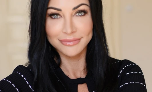 Kobieta o czarnych i długich włosach uśmiecha się, prezentując piękne brwi i usta. Ma oszałamiającą ekspresję twarzy, a stopniowe cięcie i przedłużone rzęsy dodają uroku jej urodzie.