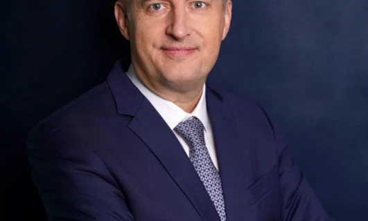 Osoba ubrana w elegancki strój z uczesanymi włosami i poważną miną. Skupienie jest na ich twarzy, kołnierzu i rękawie.