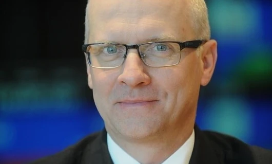 Osoba w okularach z brodą opartą na policzku i kołnierzem widocznym. Zbliżenie na okulary na twarzy.