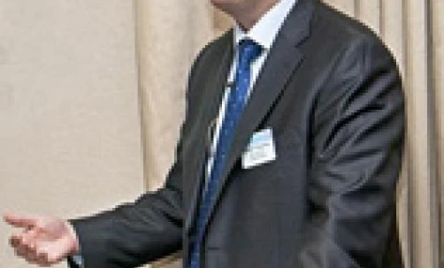 Osoba ubrana w czarny garnitur i okulary, stojąca z ręką na ramieniu. Oficjalny strój i okulary dla dopracowanego stylu.